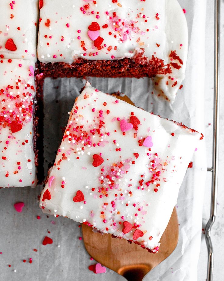 a cake with white frosting and sprinkles sitting on top of a wooden cutting board