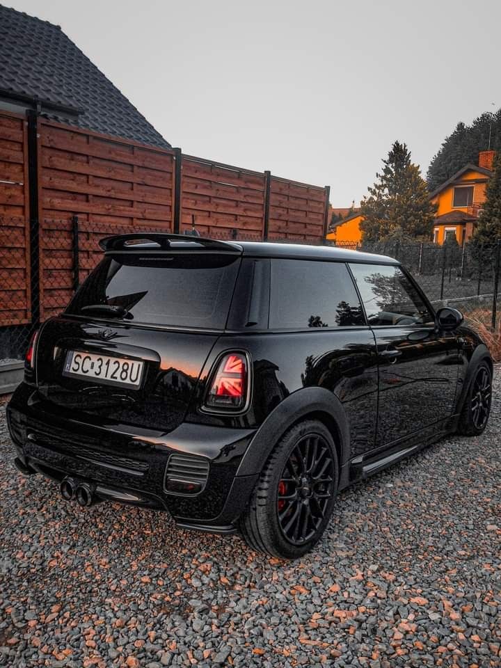 a black mini cooper parked in front of a brick wall and wooden fenced area