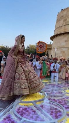 a woman in a pink and gold wedding dress walking down the street with other people watching