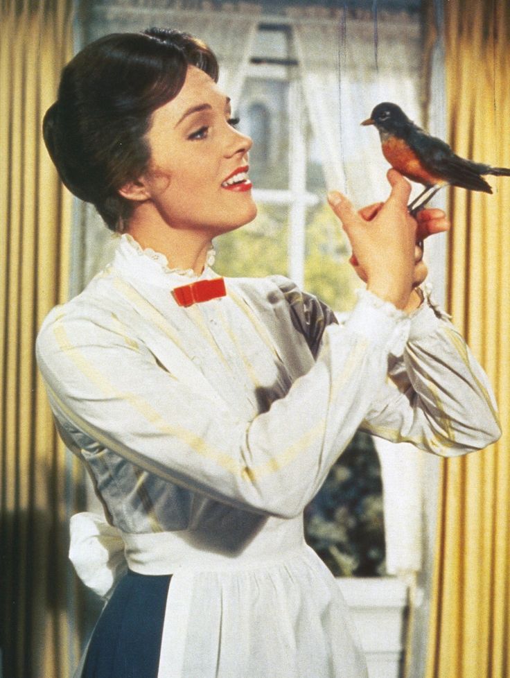 a woman holding a bird in front of her face while standing next to a window