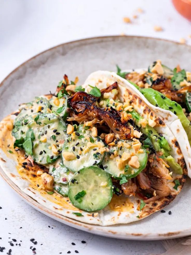 two tacos filled with meat, vegetables and sauce on top of a white plate