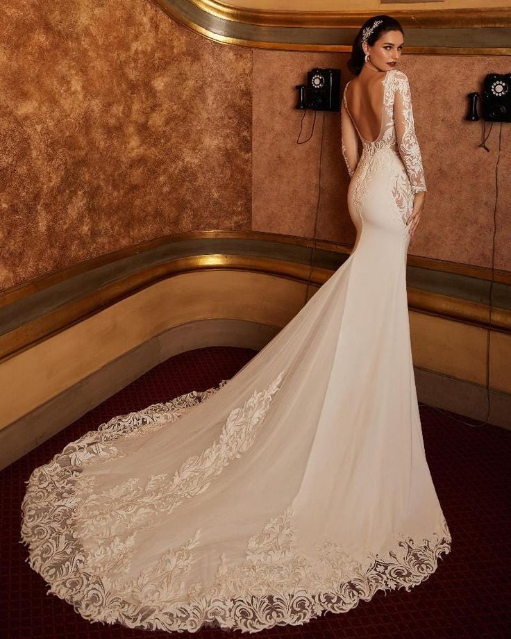 a woman in a wedding dress standing against a wall with her back to the camera