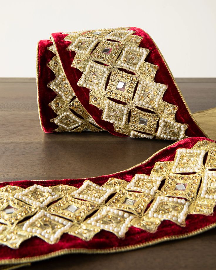 a red velvet belt with gold sequins and beads on the side, sitting on a wooden surface