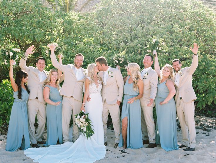 a group of people standing next to each other on top of a sandy beach with trees in the background