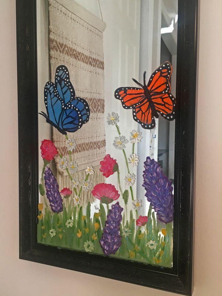 a painting of butterflies and flowers in a black frame hanging on the wall next to a window