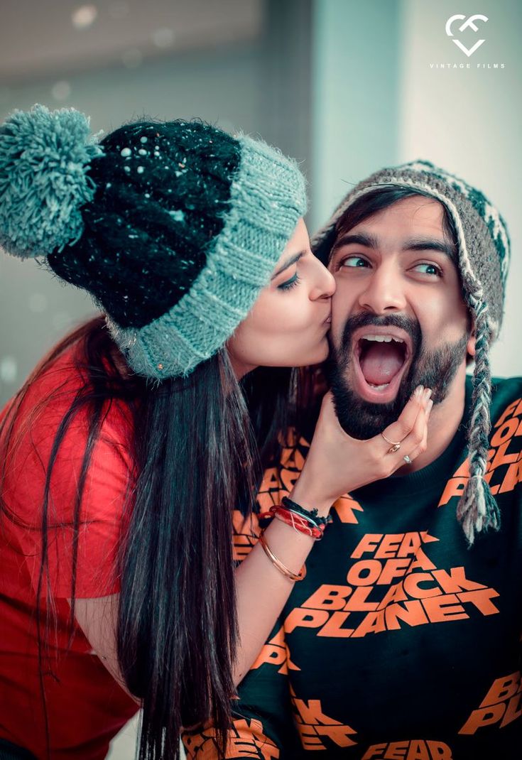 a man and woman kissing each other with their mouths wide open while wearing beanies