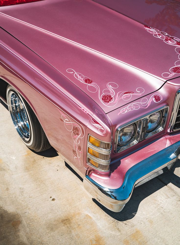 the front end of a pink car parked in a parking lot with other cars behind it