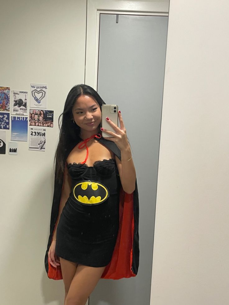 a woman taking a selfie in the bathroom wearing a batman costume and holding a cell phone