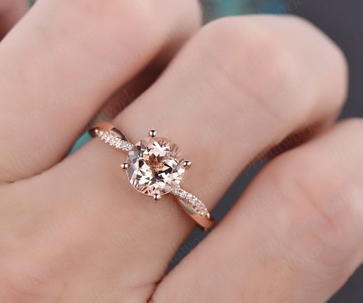 a woman's hand holding an engagement ring with a morganite and diamond band