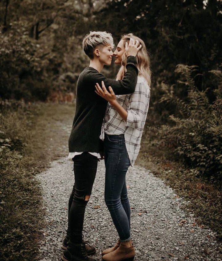 two people standing on a dirt road in the woods, one is kissing the other