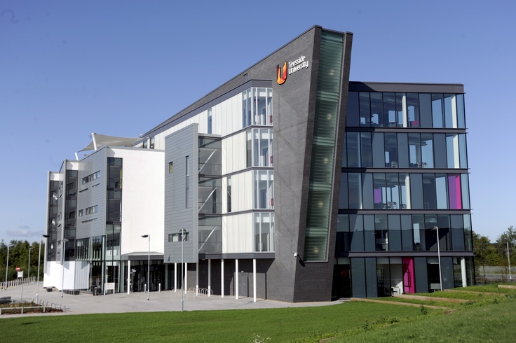 an office building with many windows and balconies on the outside, in front of a grassy area