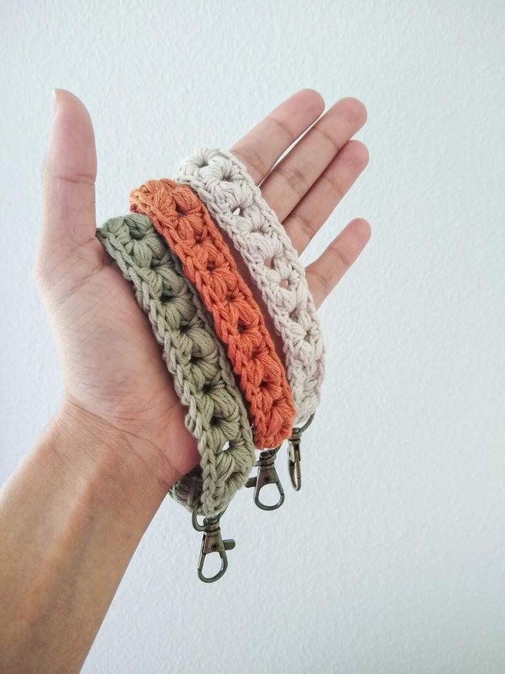 a hand is holding three bracelets in different colors and sizes, each with an adjustable loop