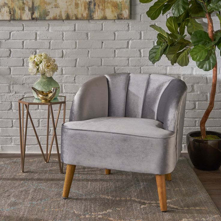 a grey chair sitting next to a potted plant on top of a rug in front of a white brick wall