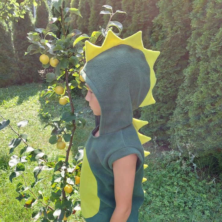 a young child wearing a dinosaur costume standing next to a tree with fruit on it