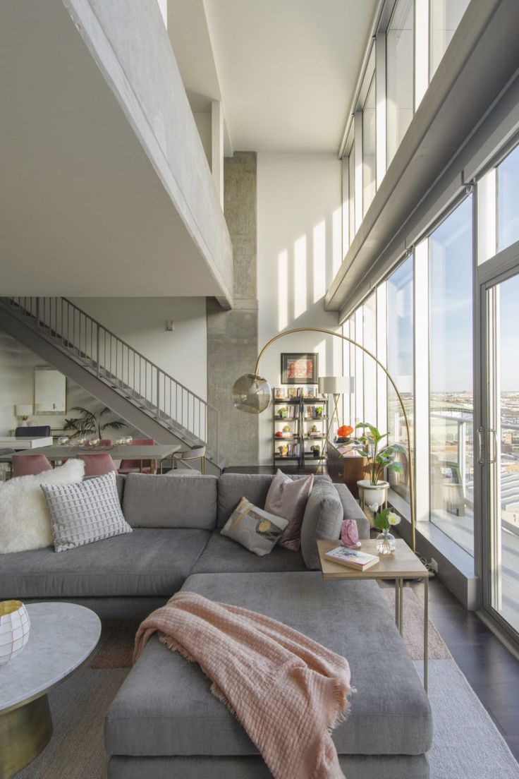 a living room filled with lots of furniture and large windows next to a stair case