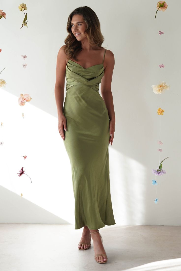 a woman wearing a green dress standing in front of a wall with flowers on it