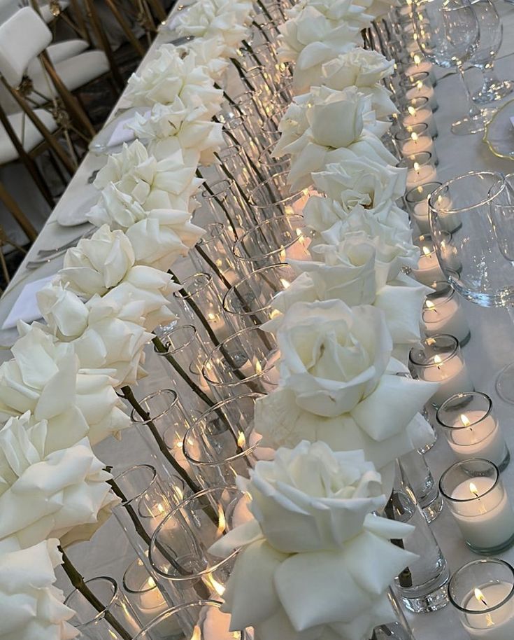 white roses and candles are lined up on a long table in front of the chairs