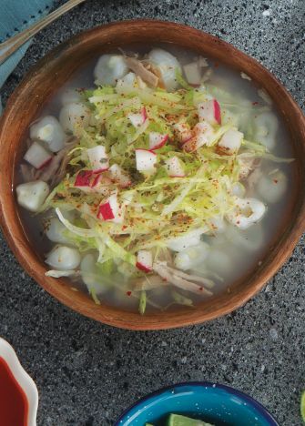 a wooden bowl filled with food next to bowls of dipping sauce