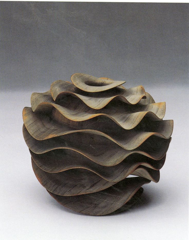 a wooden bowl with wavy designs on the top and bottom, sitting on a white surface