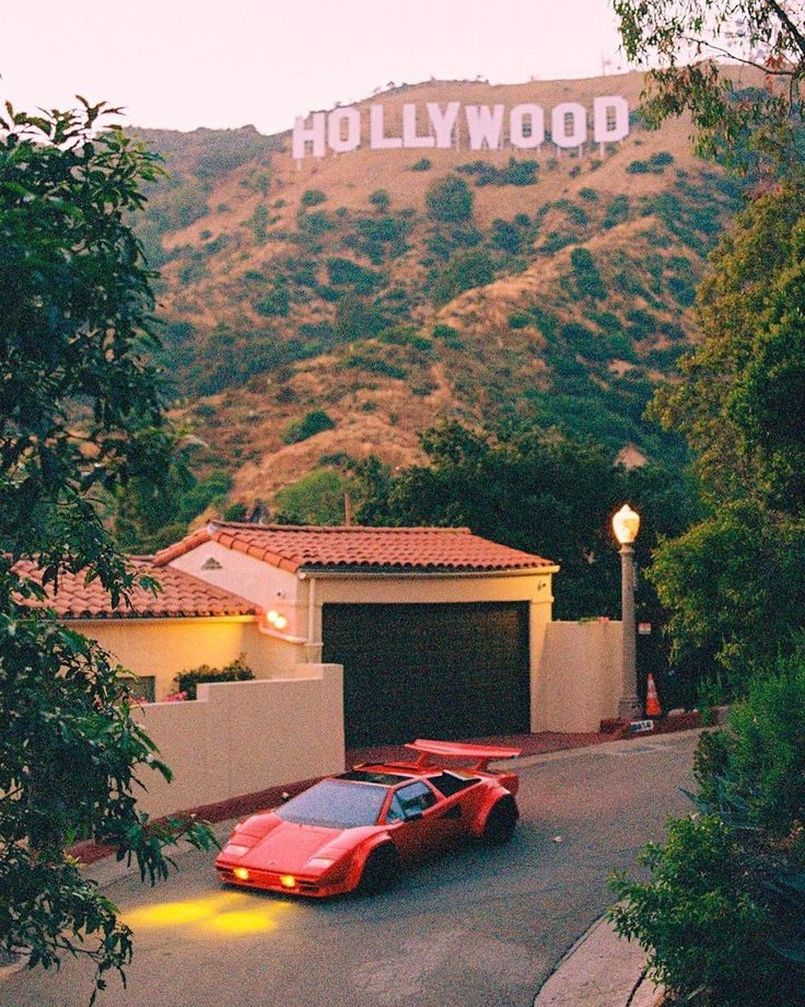 a red sports car parked in front of a hollywood sign on the side of a road