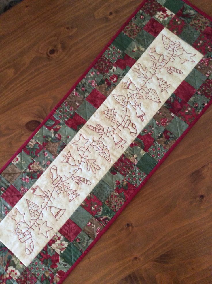 a quilted table runner with red and green designs on it sitting on a wooden floor