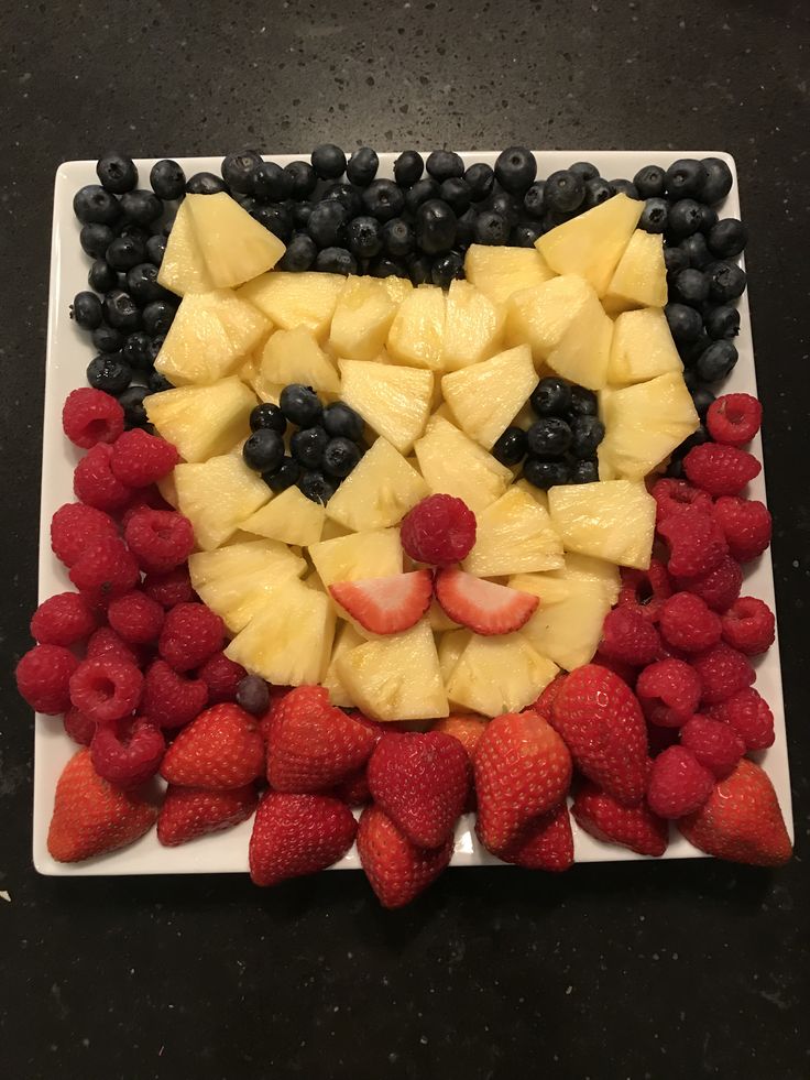 a white plate topped with fruit shaped like a cat's face on top of pineapples and raspberries