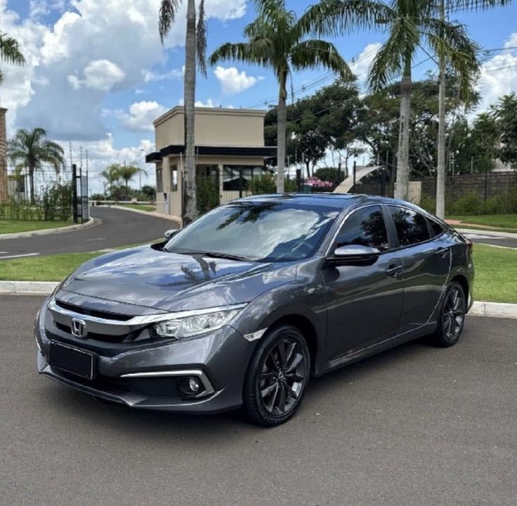 a gray honda civic is parked in front of a building with palm trees around it