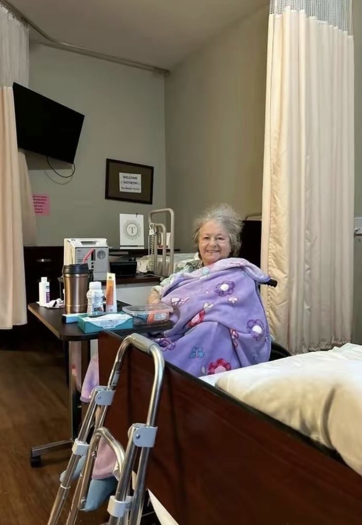 an elderly woman in a hospital bed with her hand on the rail and smiling at the camera