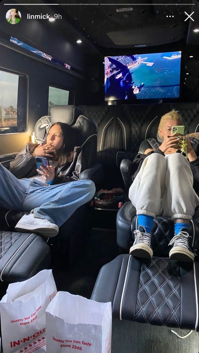 two people sitting on seats in the back of a bus with their feet up and one person holding a cell phone