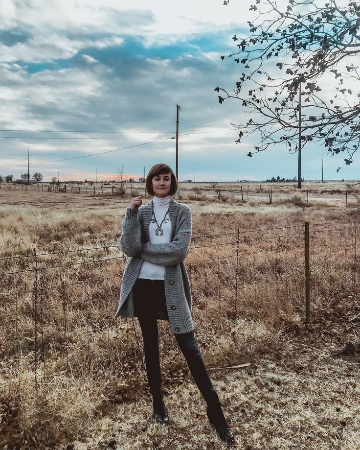 a woman is standing in the middle of a field with her arms crossed and looking at the camera