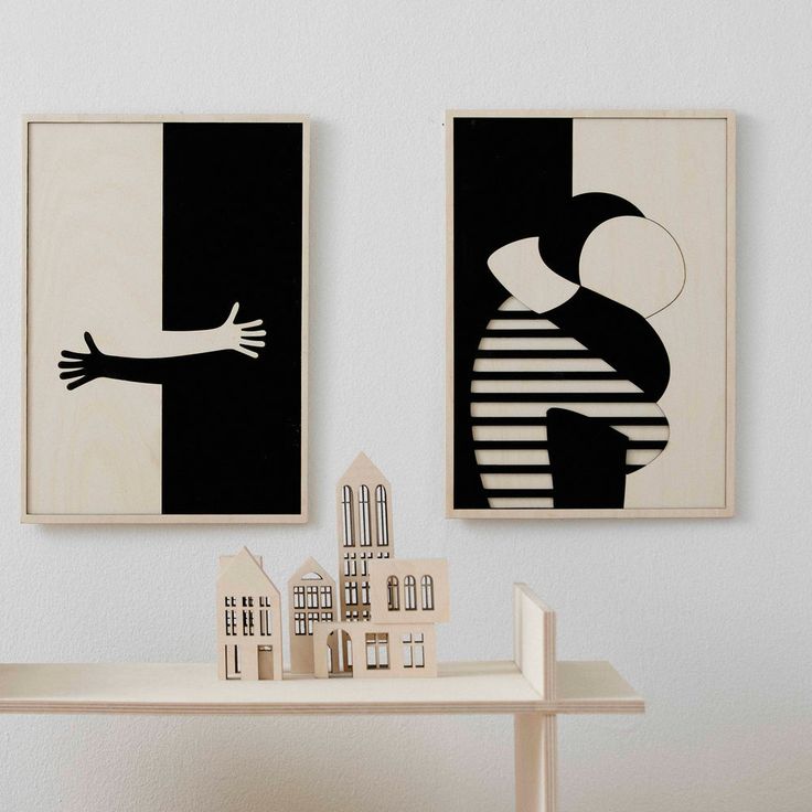 two black and white paintings hang on the wall next to a table with doll houses