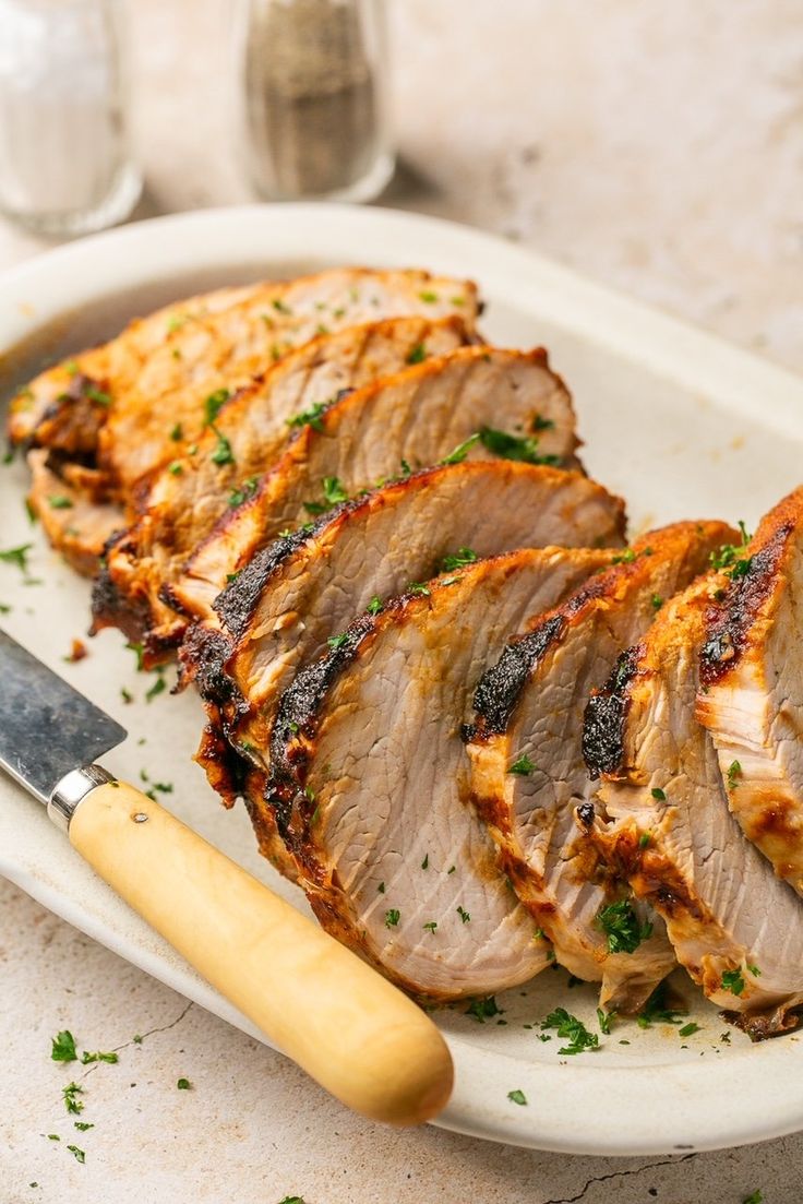 sliced pork on a plate with a knife and glass of water in the back ground