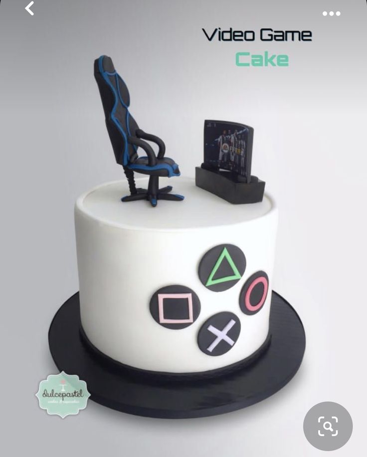 a white cake with black and blue decorations on it's top, sitting in front of a computer chair