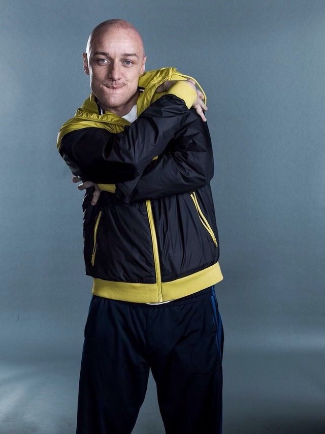 a man with his arms crossed standing in front of a gray background wearing a yellow and black jacket