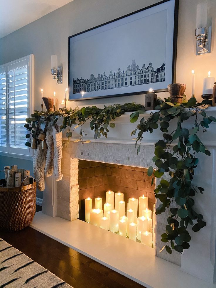 candles are lit in front of a fireplace with greenery on the mantels