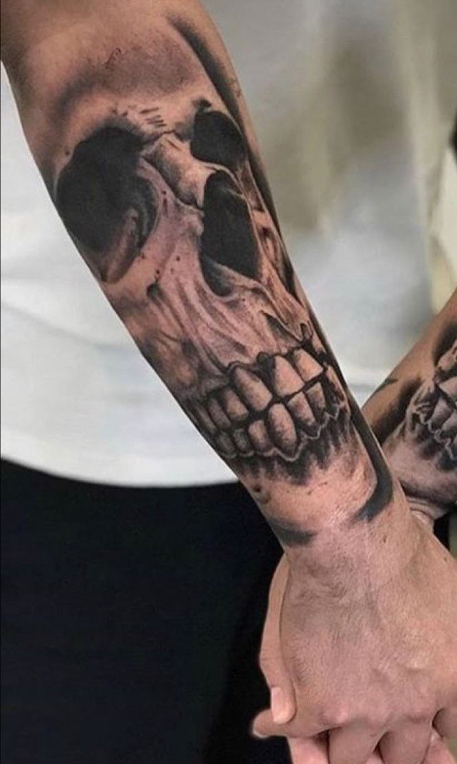 two people holding hands with tattoos on their arms and one has a skull in the middle