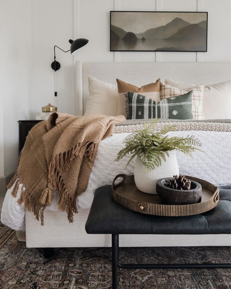 a bed with pillows and blankets on top of it next to a tray with a potted plant