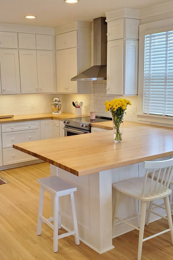 a kitchen with white cabinets and wooden counter tops, two stools at the island