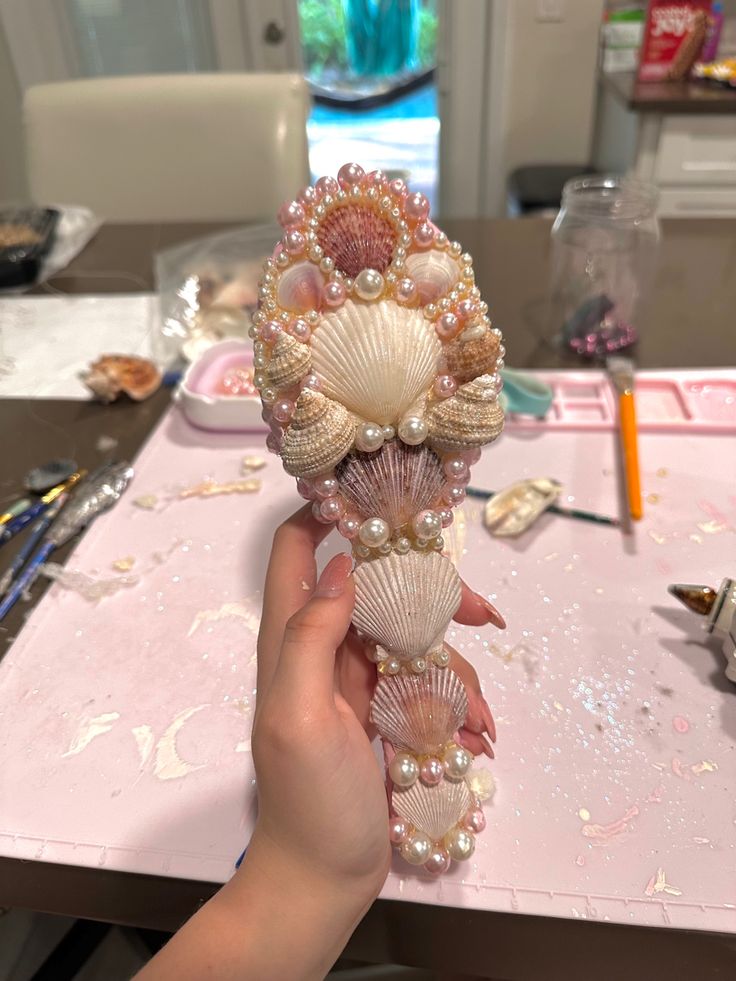 a hand holding some seashells on top of a pink table with confetti