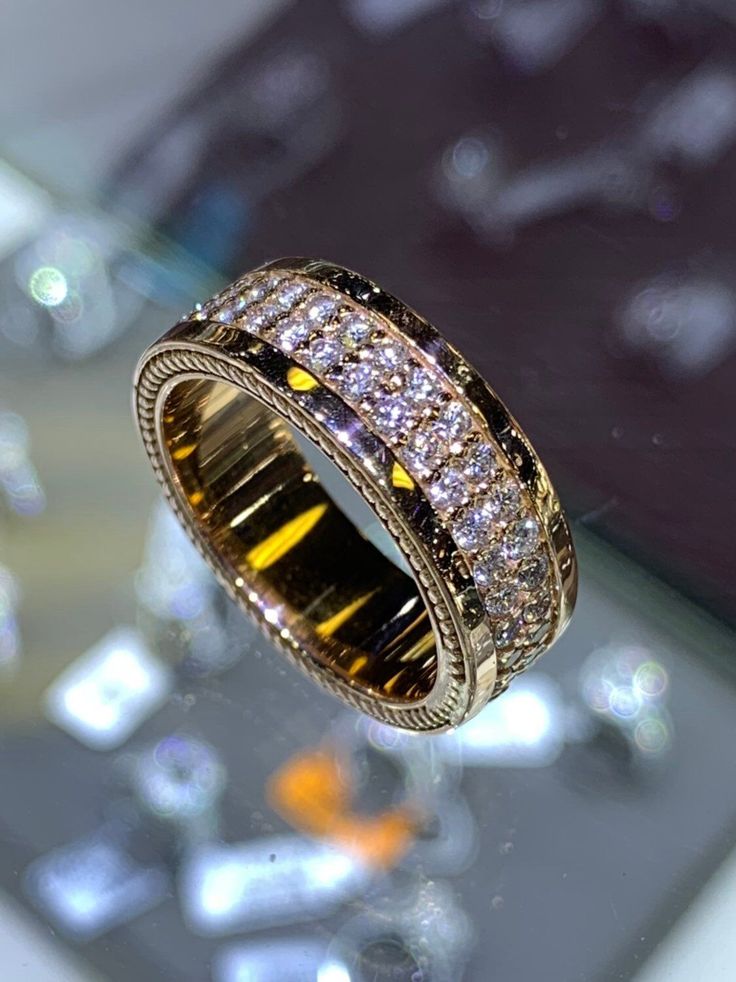 a gold ring with white and yellow diamonds on it's side sitting on a table