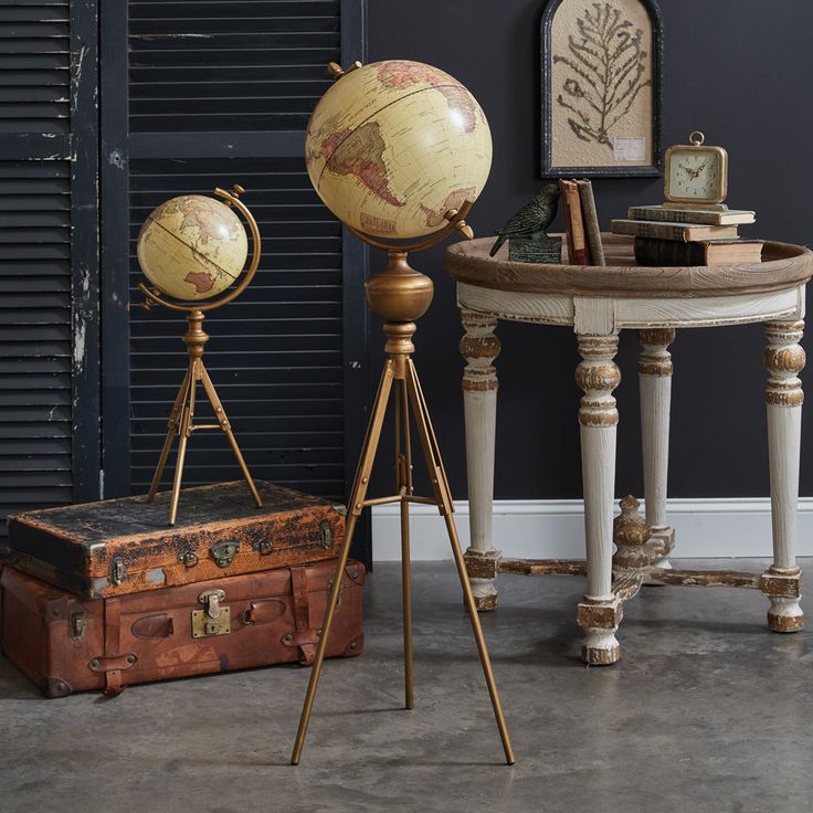 three antique globes and an old suitcase are sitting in front of a blue wall