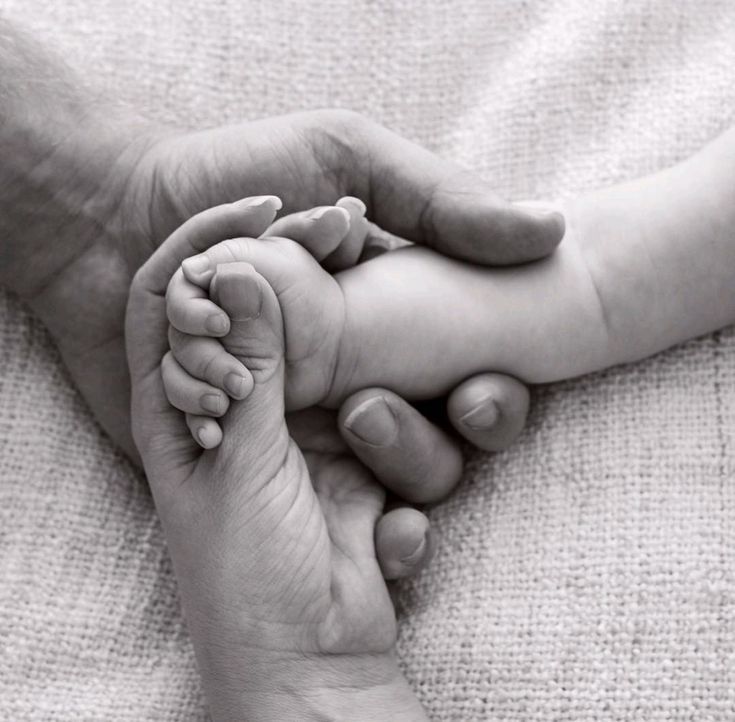 a black and white photo of a person holding a baby's hand