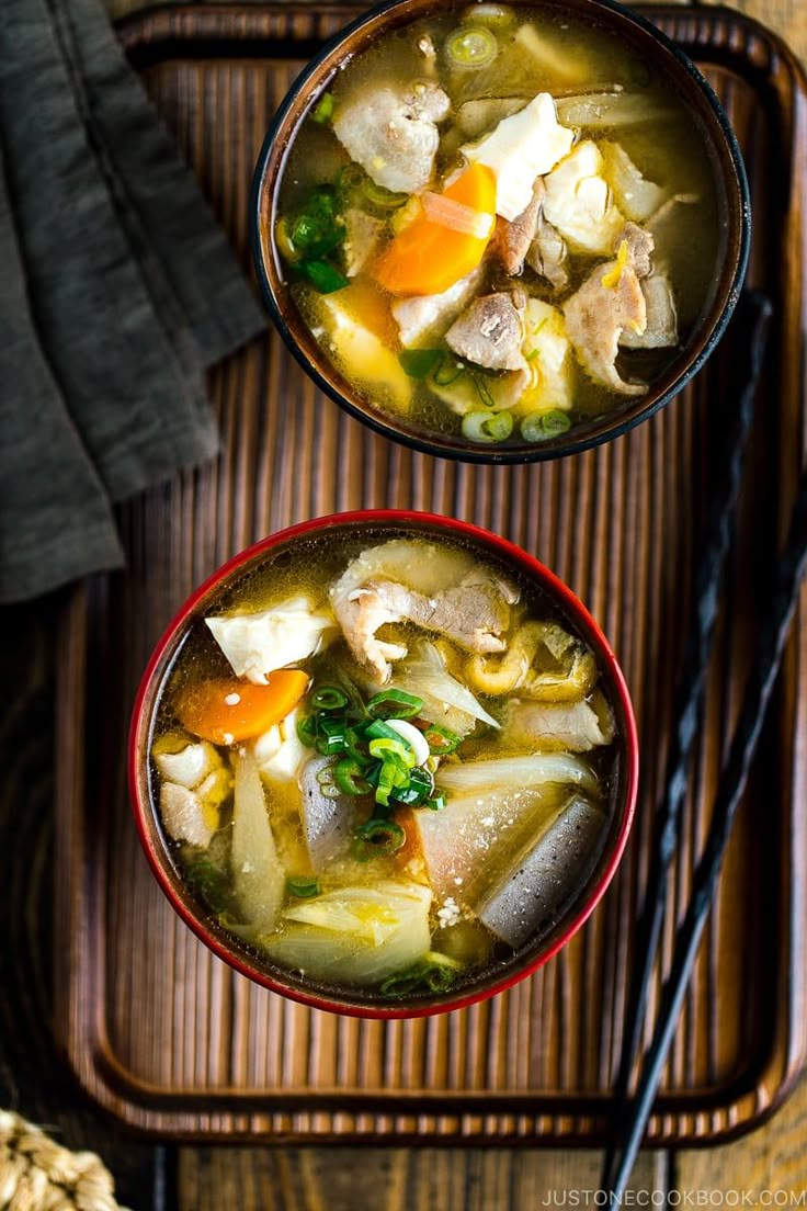 two bowls of soup on a tray with chopsticks next to each other,