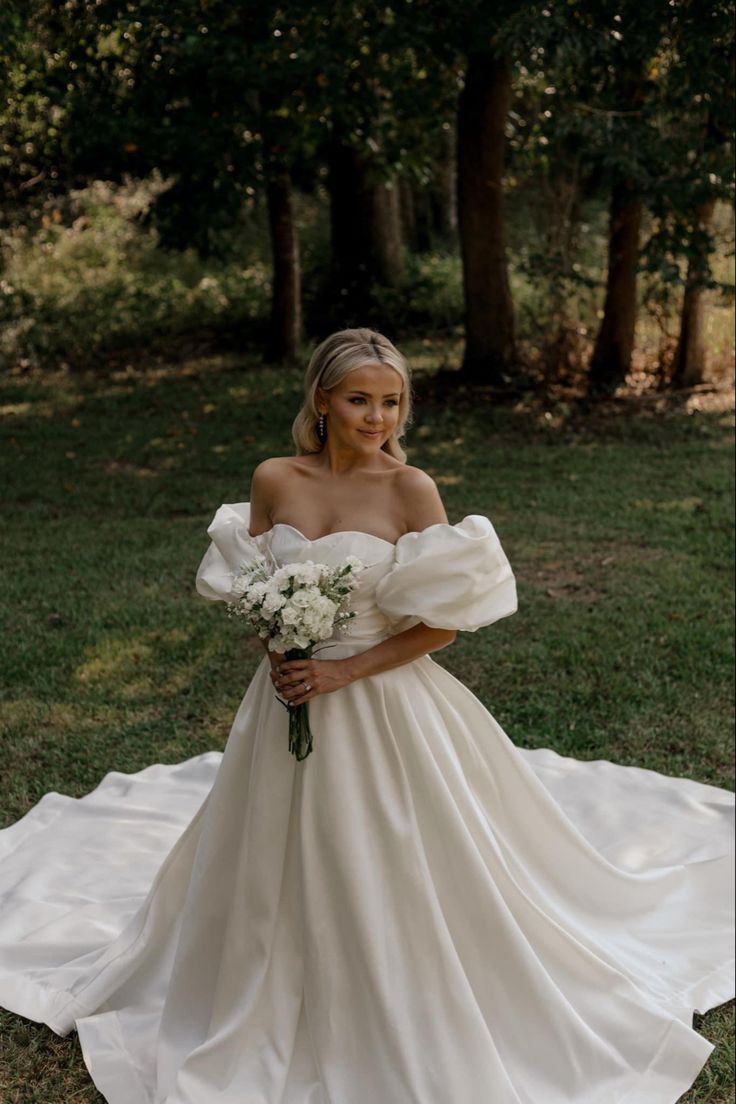 a woman in a white wedding dress standing on the grass with her arms around her waist