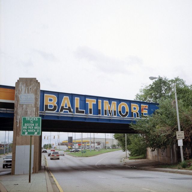 a sign that reads baltimore on the side of a bridge over a street with cars driving under it