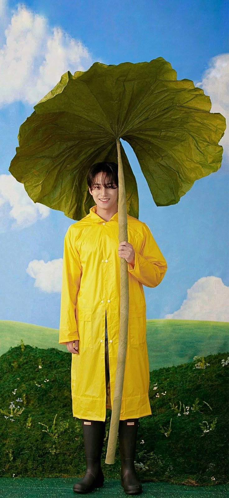 a man in yellow raincoat holding an umbrella over his head with grass and blue sky behind him