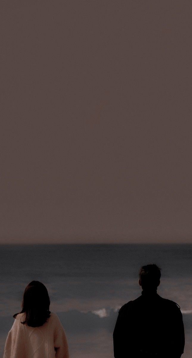 two people standing on the beach looking at the ocean