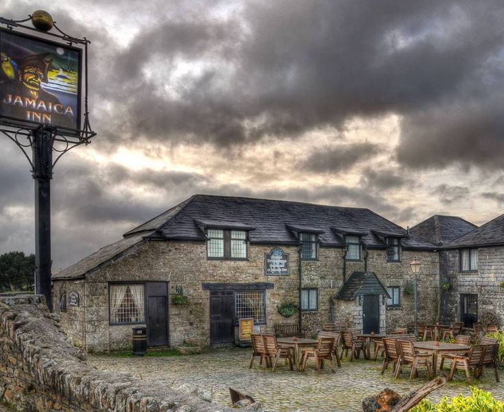 a stone building with tables and chairs in front of it under a cloudy blue sky