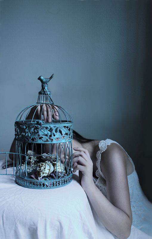 a woman laying on top of a bed next to a bird cage