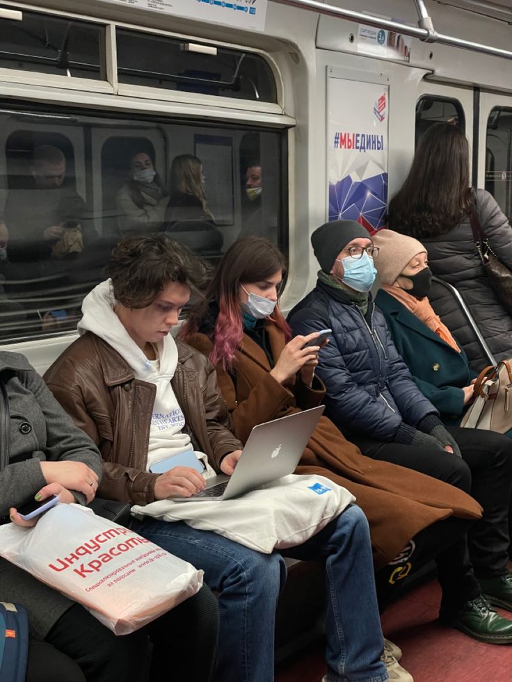 people sitting on a subway train wearing masks and using their laptops to check the time